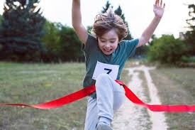 A child joyously bursts through the tape of the finish line of a race.